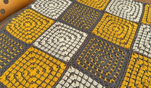 A colorful crochet patchwork blanket made of granny square motifs, displayed on a wooden table